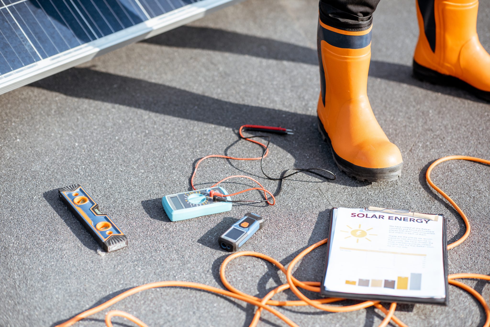 Installing solar panels, close-up on a working tools. wires and man in protective clothing standing on a rooftop with photovoltaic power station